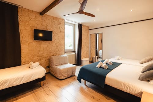 Chambre familiale de l'Hôtel Savoy à Le Bourget-du-Lac avec deux lits, coin salon confortable, murs en liège et télévision écran plat