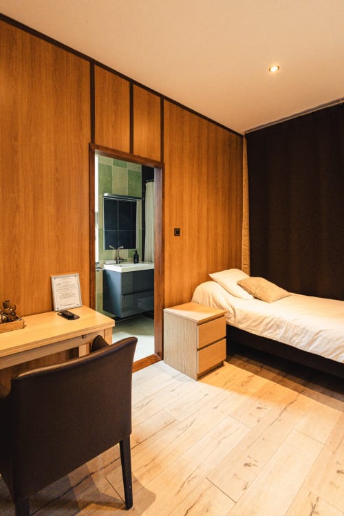 Chambre moderne du Savoy Hôtel avec boiseries, lit aux oreillers dorés, bureau et salle de bain attenante visible
