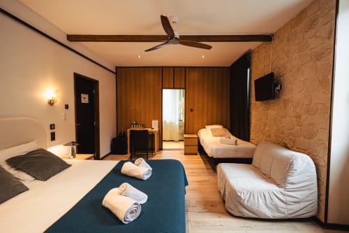 Chambre familiale de l'Hôtel Savoy au Bourget-du-Lac avec plusieurs lits, armoire en bois, téléviseur et mur d'accent en liège