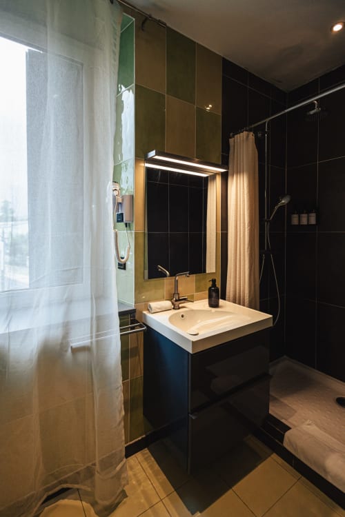Salle de bains moderne de l'Hôtel Savoy avec murs en carrelage noir, miroir éclairé, lavabo blanc et douche au Bourget-du-Lac