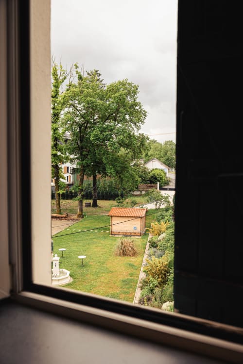 Vue depuis une chambre du Savoy Hôtel sur un jardin paysagé avec pelouse, cabanon en bois et arbres à Le Bourget-du-Lac