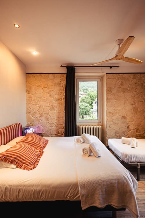 Chambre triple du Savoy Hôtel à Le Bourget-du-Lac avec murs en pierre, deux lits et ventilateur de plafond