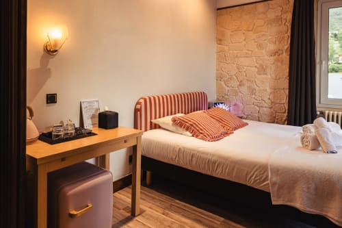 Chambre triple confortable du Savoy Hôtel avec tête de lit rayée, bureau, éclairage chaleureux et mur en pierre apparente à Le Bourget-du-Lac.