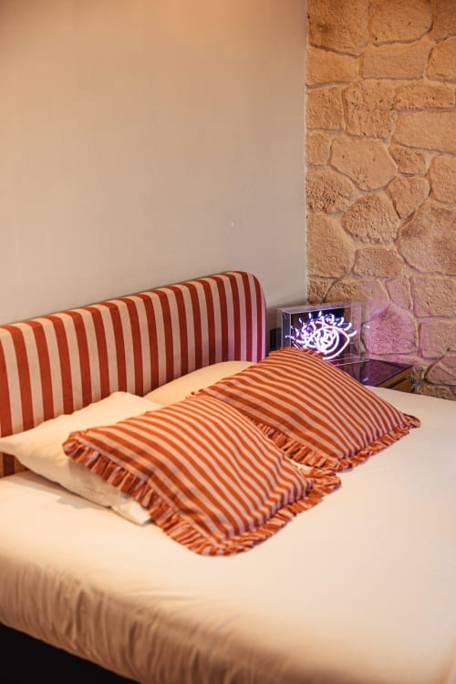 Chambre moderne au Savoy Hôtel avec coussins rayés rouge et blanc, mur en pierre et décoration enseigne néon