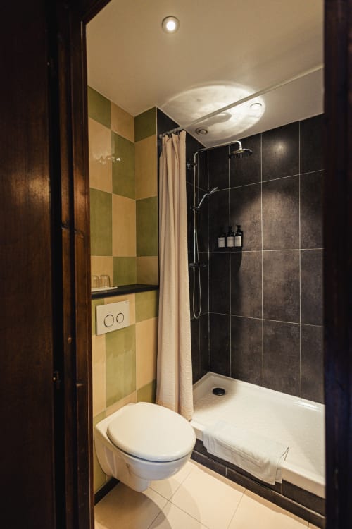 Salle de bain moderne du Savoy Hôtel : toilettes blanches, douche carrelée noire, mur d'accent vert et éclairage suspendu.
