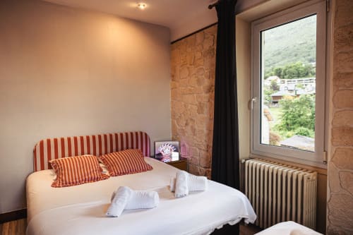 Chambre triple confortable au Savoy Hôtel avec tête de lit rayée rouge, vue sur les montagnes et murs en pierre apparente