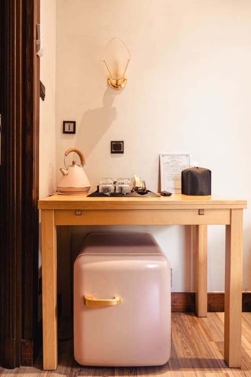 Kitchenette de l'Hôtel Savoy avec bureau en bois, mini-réfrigérateur rose, bouilloire et applique murale