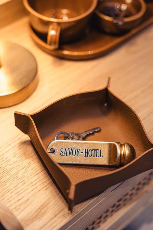 Porte-clé vintage en laiton du Savoy Hôtel dans un étui en cuir sur un bureau en bois