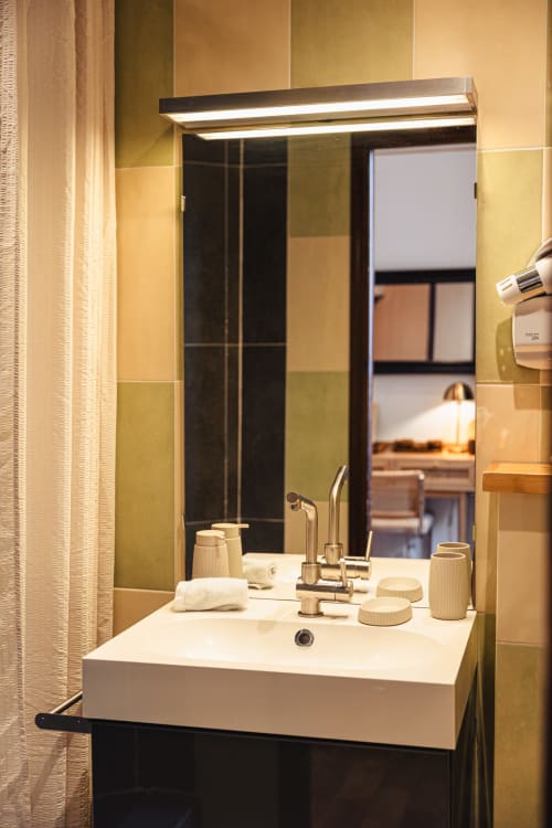 Salle de bains moderne au Savoy Hôtel avec lavabo blanc, robinetterie chromée, miroir à éclairage LED et murs carrelés beige