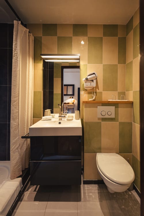 Salle de bains moderne au Savoy Hôtel avec carrelage damier vert, lavabo blanc, toilettes et miroir rétroéclairé
