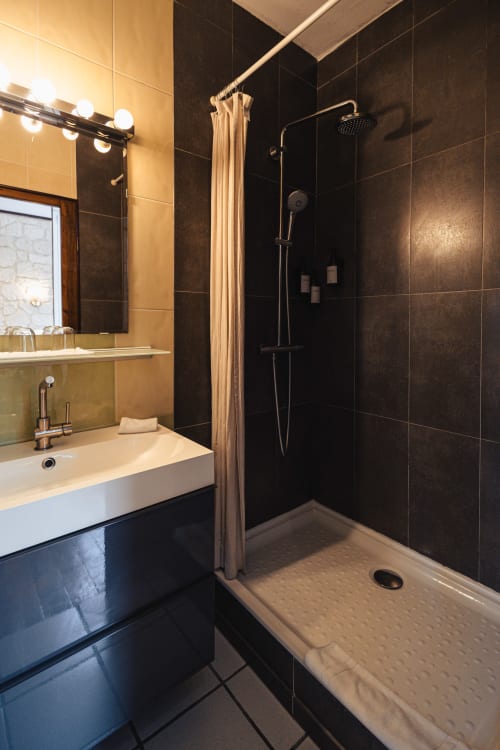 Salle de bains moderne à l'hôtel Savoy avec douche carrelée noire, lavabo blanc et miroir lumineux au Bourget-du-Lac