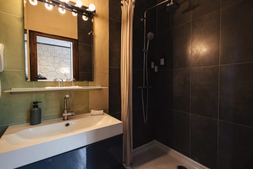 Salle de bain moderne du Savoy Hôtel avec lavabo blanc, douche spacieuse carrelée foncée et miroir de vanité éclairé