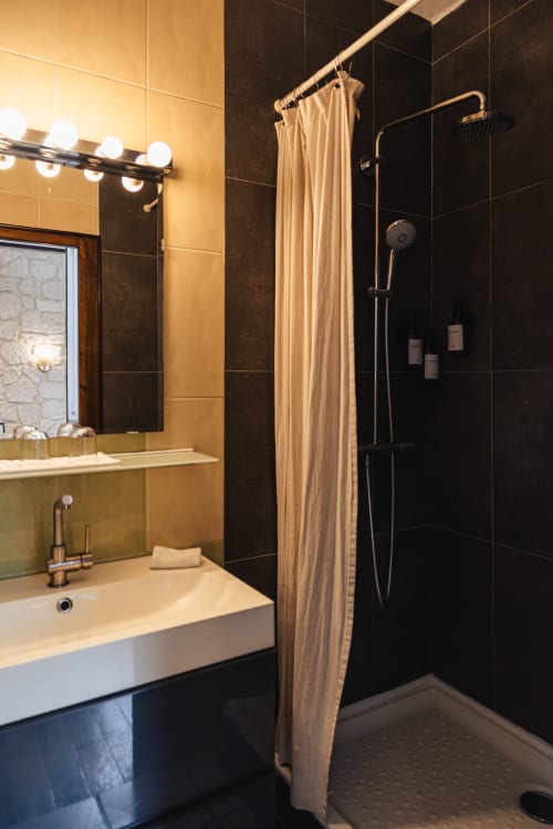 Salle de bains moderne du Savoy Hôtel avec douche en carrelage noir, vasque beige et robinetterie en laiton