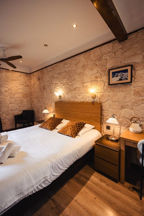 Chambre double cosy du Savoy Hôtel avec murs en pierre, mobilier bois et éclairage chaleureux au Bourget-du-Lac