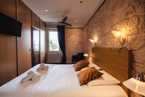 Chambre double de l'Hôtel Savoy aux murs en pierre apparente, tête de lit en bois, coussins léopard et vue montagne