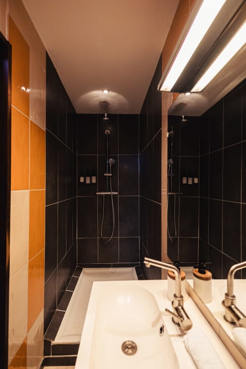 Salle de bains double moderne au Savoy Hôtel Le Bourget-du-Lac avec double vasque, carrelage noir et cabines de douche séparées