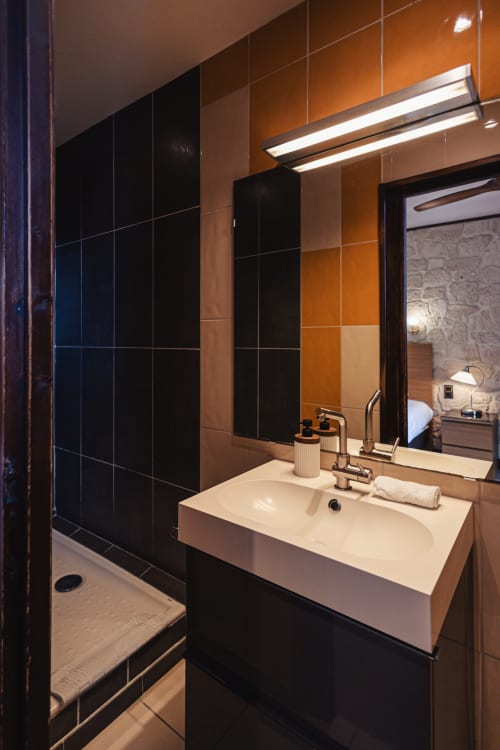 Salle de bains moderne de l'hôtel Savoy avec lavabo blanc, accents carrelage noir et luminaires contemporains