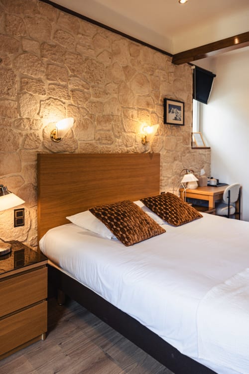 Chambre double du Savoy Hôtel au Bourget-du-Lac avec murs en pierre, lit en bois et éclairage ambiant