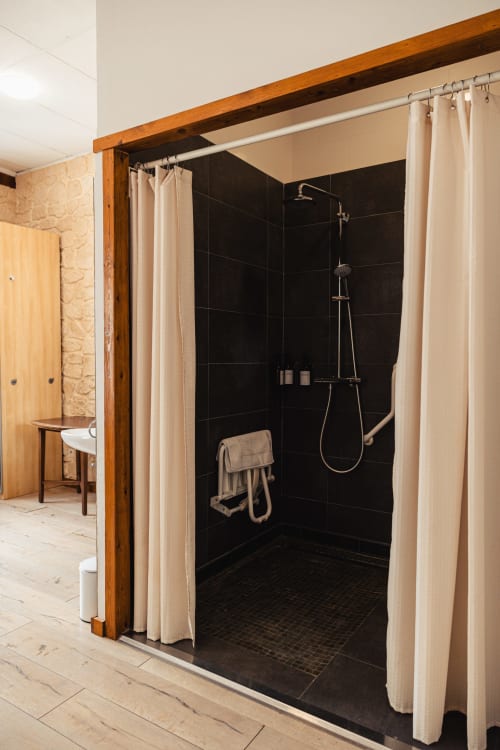 Douche moderne aux murs en carrelage noir et rideaux crème à l'hôtel Savoy du Bourget-du-Lac, France