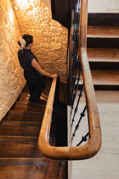 Femme montant l'escalier en bois du Savoy Hôtel Le Bourget-du-Lac avec mur en pierre illuminé