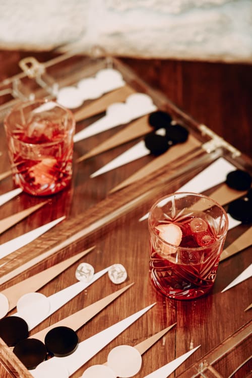 Mise en place cocktail du Savoy Hôtel avec verre de boisson rouge, jeu de backgammon et pions sur table en bois