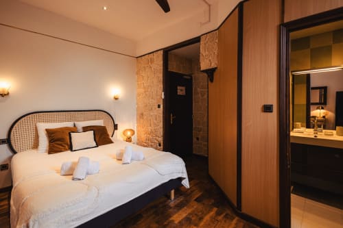 Chambre moderne de l'Hôtel Savoy avec lit blanc, tête de lit en rotin et salle de bains attenante.