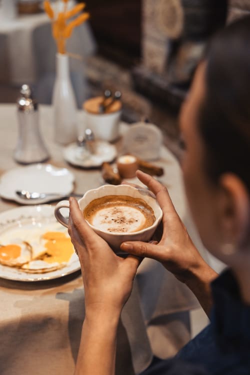 Client tenant un cappuccino au Savoy Hôtel Le Bourget-du-Lac, avec table de petit-déjeuner et pâtisseries