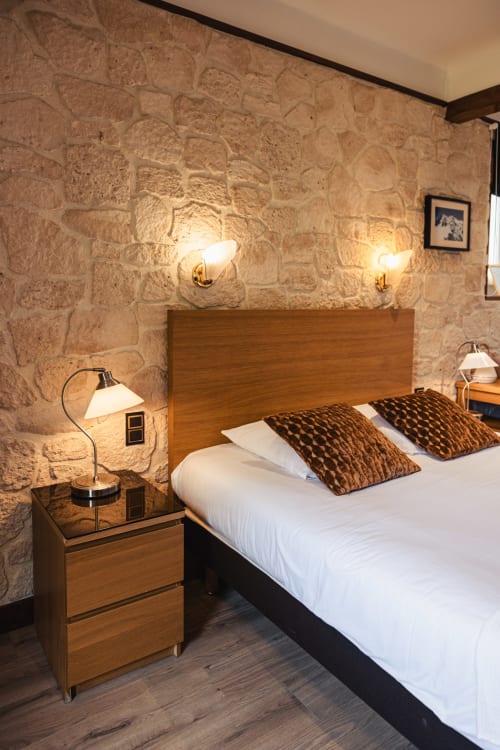 Chambre douillette au Savoy Hôtel avec murs en pierre, lit en bois, coussins marron et éclairage ambiant au Bourget-du-Lac