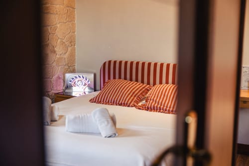 Chambre de l'Hôtel Savoy Le Bourget-du-Lac avec oreillers rouges rayés, literie blanche et détail de mur en pierre