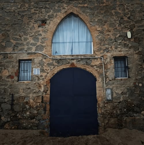 Façade en pierre d'un immeuble côtier à Palafrugell avec portail cintré sombre et fenêtre aux volets bleus