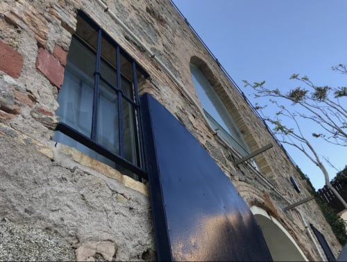 Façade en pierre d'un appartement en bord de mer à Palafrugell avec fenêtre à encadrement bleu et accès à la vue sur la mer