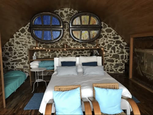 Chambre cosy d'un appartement face à la mer à Palafrugell avec murs en pierre, deux fenêtres rondes, lit queen, accents turquoise