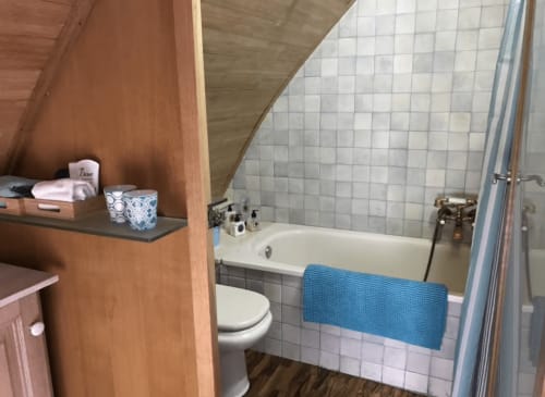 Salle de bain moderne dans un appartement de Palafrugell avec carrelage blanc, baignoire, toilettes et étagères en bois pour les articles de toilette
