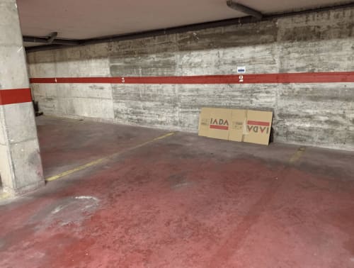 Parking souterrain du complexe Finques Garcia Enrich à Palafrugell avec sol rouge, murs en béton et places numérotées