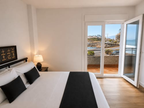 Moderno dormitorio con balcón vistas al mar en el apartamento As Estelas, Baiona. Cama doble con acentos negros y vistas al océano.