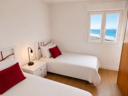 Dormitorio moderno en apartamento de Baiona con camas gemelas, ventanas con vistas al mar y playa, detalles en rojo