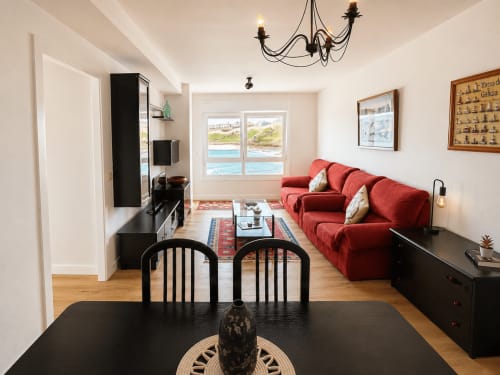 Sala de estar moderna con vista al mar en Baiona, sofá rojo, comedor y vistas al océano desde las ventanas