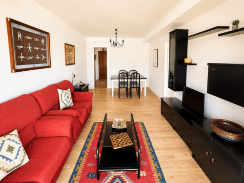 Amplio salón en el apartamento As Estelas de Baiona con sofá rojo, mueble de entretenimiento negro, comedor y suelos de madera