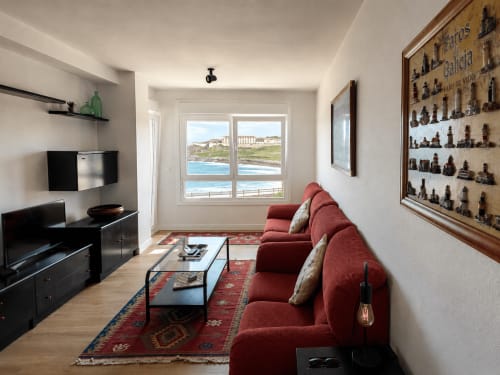 Amplio salón con vistas al mar en apartamento de Baiona, sofá rojo, TV y vistas costeras