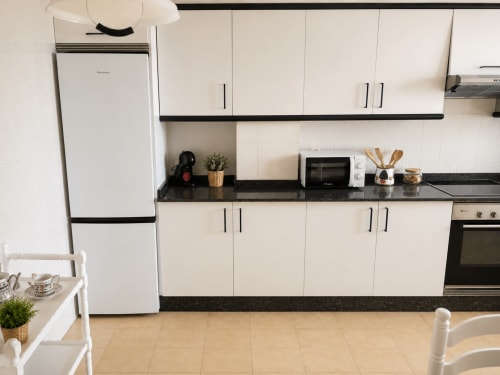 Cocina moderna del apartamento As Estelas en Baiona con muebles blancos, encimeras negras y electrodomésticos de acero inoxidable