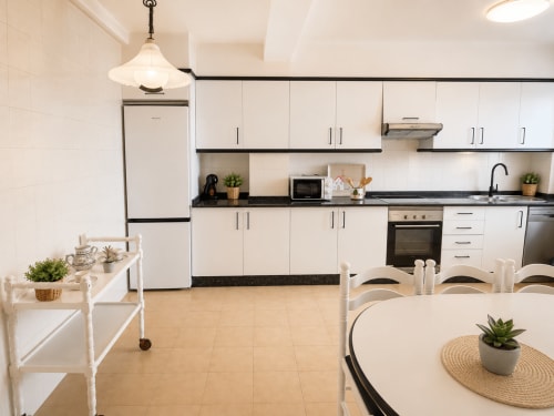 Cocina moderna en el apartamento As Estelas de Baiona con muebles blancos, encimeras negras, electrodomésticos de acero inoxidable y comedor