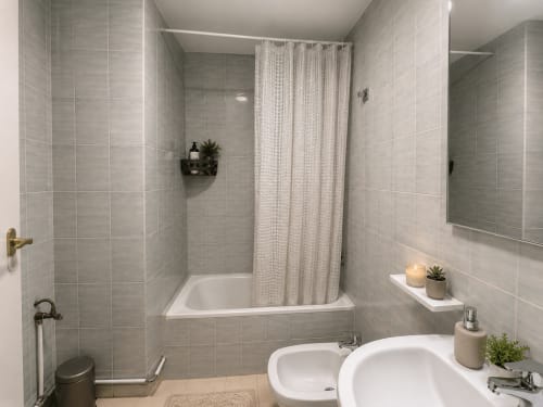 Baño moderno en apartamento As Estelas, Baiona con doble lavamanos, bañera, ducha, paredes de azulejos grises y vistas al mar