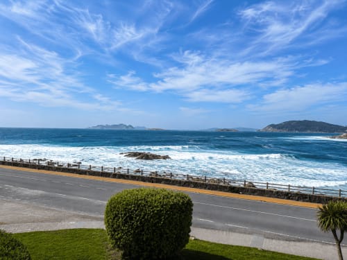 Vista desde balcón del apartamento de Baiona: paisaje costero con olas, acantilados y césped verde frente al Atlántico