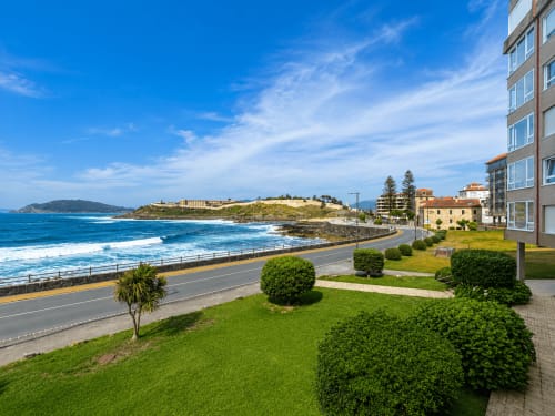 Apartamento en primera línea de playa de Baiona con vistas al mar, jardines cuidados y acantilados costeros bajo cielo azul