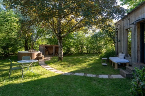 Vue intime du gîte La cabane au bain avec terrasse, bain à remous et verdure luxuriante aux Cabanes de Julie