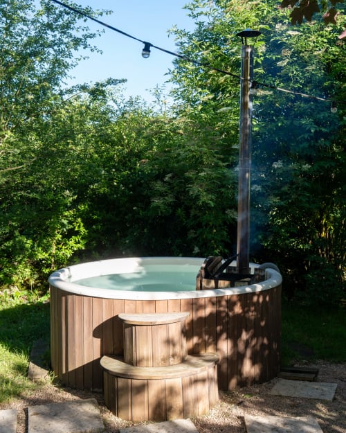 Bain à remous en bois aux eaux turquoise, entouré de verdure luxuriante aux Cabanes de Julie, Lissac-et-Mouret