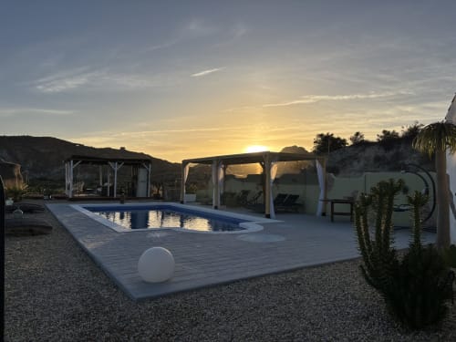 Pôr do sol sobre a piscina El Sueño em Huércal-Overa com pérgolas, água azul, vistas de montanhas e paisagem desértica