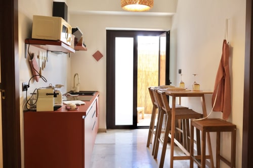 Cucina e zona dining moderna nel mini appartamento Tagasuites a Catania con mobili rossi, tavolo in legno e porte in vetro