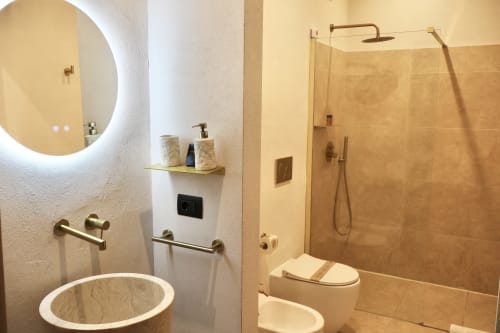 Bagno moderno nell'appartamento Tagasuites di Catania con specchio illuminato rotondo, rubinetteria in ottone, doccia walk-in e wc