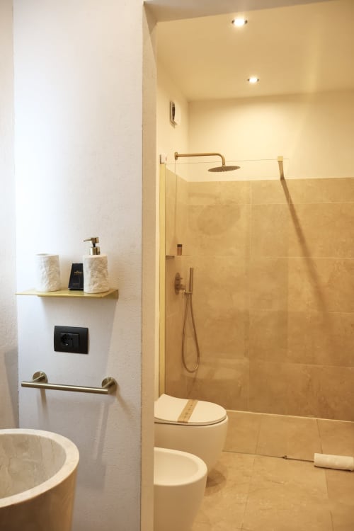 Bagno moderno di Tagasuites Catania con doccia walk-in, toilet, vanity con rubinetteria in ottone e illuminazione calda